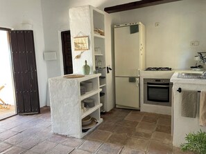 Cozinha compacta com geladeira embutida, fogão e pia. Há prateleiras com louças e um quadro pendurado.