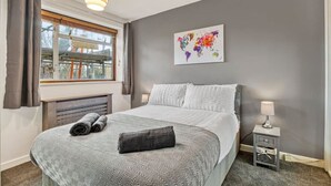 Een slaapkamer met een bed, een raam met gordijnen, een radiator, een nachtkastje met een lamp en een wereldkaart als decoratie aan de muur.