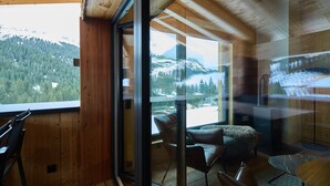 Een houten interieur met een glazen deur die uitkomt op een balkon met uitzicht op de bergen.