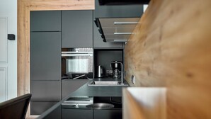 A modern kitchen with dark cabinetry, a coffee machine, and a wooden accent wall.