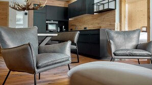A modern living room with two grey leather sofas, a wooden floor, and a kitchen in the background.