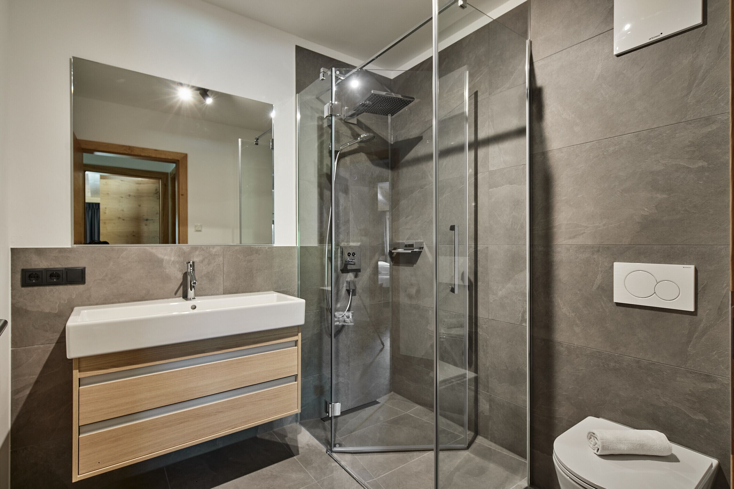A modern bathroom with a glass-enclosed shower, a wooden vanity with a white sink, and a toilet with a towel on it.
