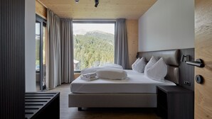Ein modernes Schlafzimmer mit einem großen Bett, Holzboden und Blick auf einen bewaldeten Berg.