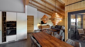 Eine moderne Küche mit integrierten Geräten, ein Essbereich mit Holztisch und eine gemütliche Sitzecke mit Sofa und Sesseln.