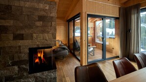 Tunnelmallinen mökin sisustus, jossa on kivinen takka, puuseinät ja lasiovi, joka johtaa terassille.