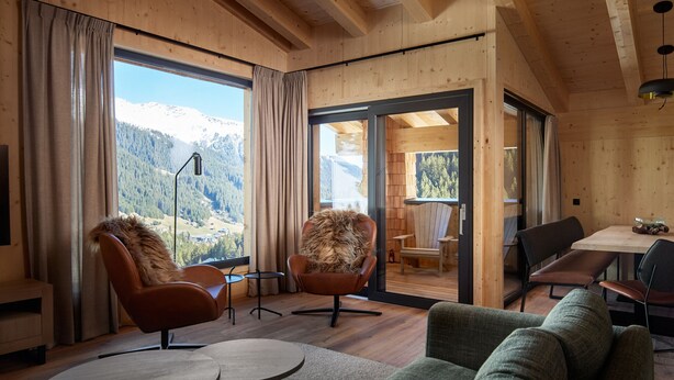 A wooden interior with a large window, two leather chairs, a green sofa, and a dining area. - 5805 Alm-Lodge tschintg Ski-in-out (Gargellen)