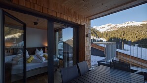 A modern hotel room with a wooden ceiling, a large glass door leading to a balcony, and a view of snow-covered mountains. - 5805 Alm-Lodge tschintg Ski-in-out (Gargellen)