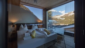 A bedroom with a large window offering a mountain view. The room has a wooden ceiling and a bed with white bedding and pillows. - 5805 Alm-Lodge tschintg Ski-in-out (Gargellen)