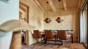 Ein Holzinnenraum mit Essbereich, inklusive Tisch und Stühlen, Holzbalken an der Decke und Pendelleuchten.