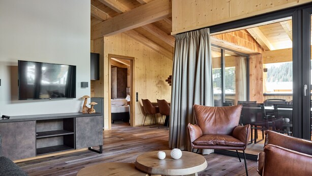 Ein modernes Wohnzimmer mit Flachbildfernseher, Ledersesseln, einem Holztisch und einer großen Schiebeglastür zum Essbereich.