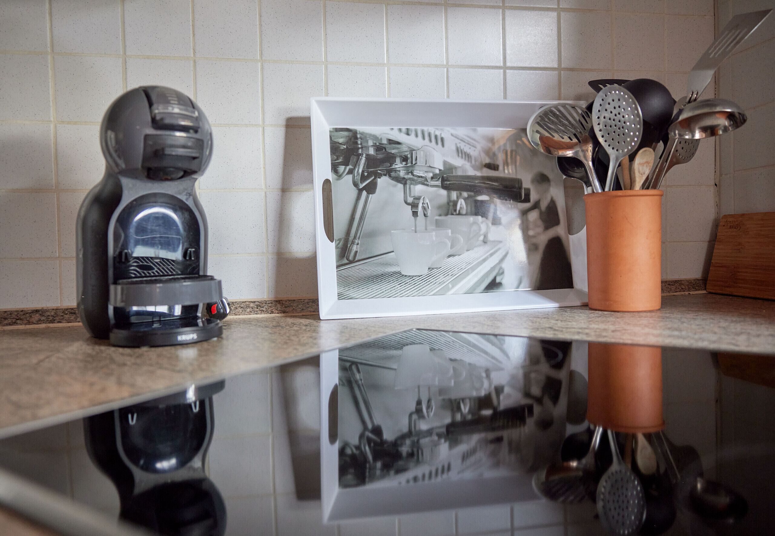 A coffee machine, a framed picture, and a container with kitchen utensils on a kitchen counter.