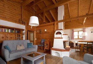 Ein gemütliches Blockhaus-Interieur mit Holzbalkendecke, Kamin, einer Couch und einem Essbereich.