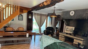 A cozy living room with a wooden staircase, a green leather sofa, a fireplace, and a dining area with wicker chairs and a table.