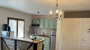 A kitchen with a stone island, green cabinets, a chandelier, and a refrigerator.
