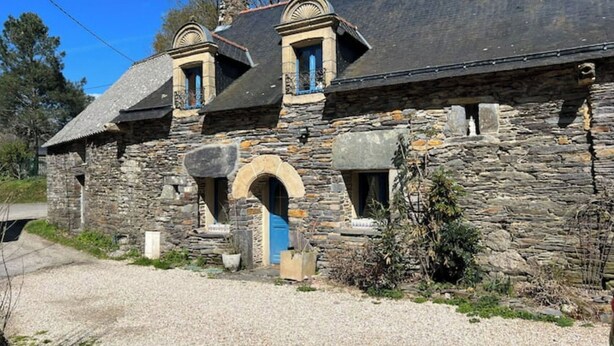 A stone building with a gravel driveway, a blue door, and a small archway.