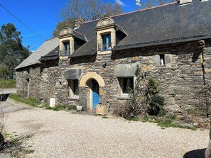 Un bâtiment en pierre avec une allée gravillonnée, une porte bleue et un petit arc d’entrée.