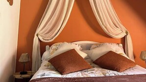 A bedroom with a bed under a wooden beam structure, orange walls, and a canopy bed with brown pillows.