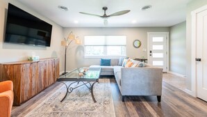 A living room with a sofa, coffee table, TV, and a ceiling fan. - Zander Haus 3 Bedroom Home by RedAwning (Fredericksburg)