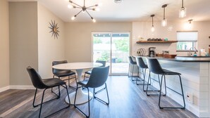 A modern kitchen with a central island, black bar stools, and a dining table with chairs. - Zander Haus 3 Bedroom Home by RedAwning (Fredericksburg)