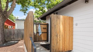 A wooden gate with a towel hanging on it, leading to a house with white siding. - Zander Haus 3 Bedroom Home by RedAwning (Fredericksburg)