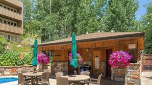 An outdoor patio with a round table and chairs, surrounded by stone walls and covered by green umbrellas. - Mtn Views a Short Walk to Lionshead Gondola, SV22A (Vail)