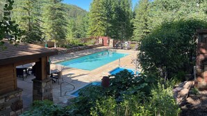 A swimming pool with a stone deck, surrounded by lush greenery and trees. - Mtn Views a Short Walk to Lionshead Gondola, SV22A (Vail)