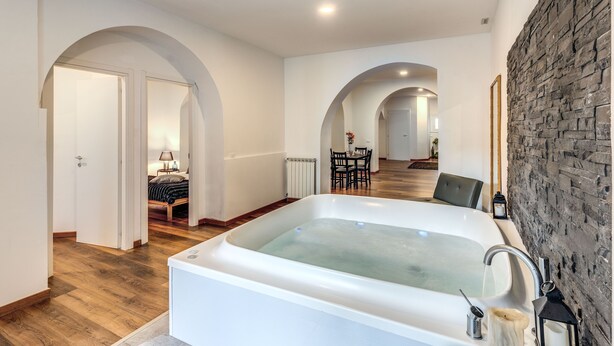 A spacious bathroom with a large bathtub, wooden flooring, and a stone wall. - Charming Loft with terrace (Roma)