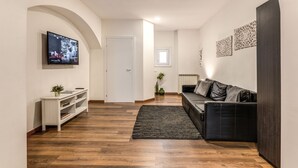 A modern living room with a flat-screen TV, a dark sofa, a white console table, and a wooden floor. - Charming Loft with terrace (Roma)