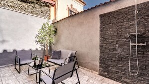 An outdoor patio with a stone-tiled floor, a seating area with two chairs and a table, a potted plant, and a stone wall with a built-in shower. - Charming Loft with terrace (Roma)