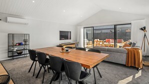 Ein geräumiges Wohnzimmer mit einem Holzesstisch, schwarzen Stühlen, einem grauen Sofa und einer großen Schiebeglasdoor zum Außenbereich.