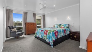 A bedroom with a bed, a chair, a dresser, and a ceiling fan. - Shores Getaway - One Tree Point Holiday Home (One Tree Point)