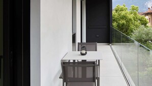 Un balcón moderno con una mesa y una silla, barandilla de vidrio y vistas a montañas.