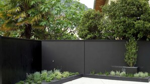 Un espacio exterior moderno con una cerca negra, diversas plantas y un cartel con el número '03'.
