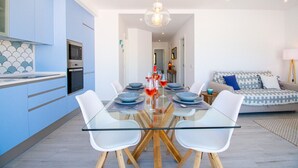 Une cuisine moderne avec des meubles de couleur bleue, une table à manger en verre et un canapé dans l’espace salon.