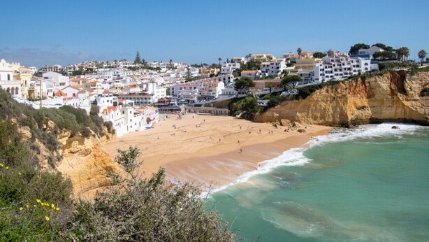 Une ville côtière avec des bâtiments construits sur une falaise surplombant une plage de sable et des eaux turquoise.