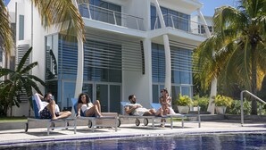 Un hotel moderno con area piscina, lettini prendisole e palme.