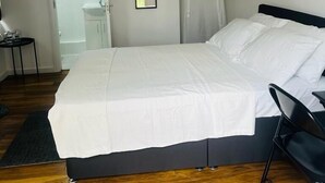 Een slaapkamer met een bed, een bureau en een zichtbare badkamer door een open deur.