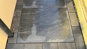 Een nat betegeld pad met een houten hek en een gele muur.