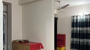 A room with a wooden wardrobe, a red chair, a ceiling fan, and a patterned curtain. - Appayan Guest House Baridhara (Dhaka)