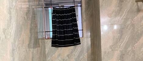 A small bathroom with a toilet, a shower, and a window with a black curtain.