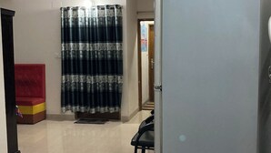 A hallway with a tiled floor, a ceiling fan, a red cushioned bench, a patterned curtain, and a refrigerator. - Appayan Guest House Baridhara (Dhaka)