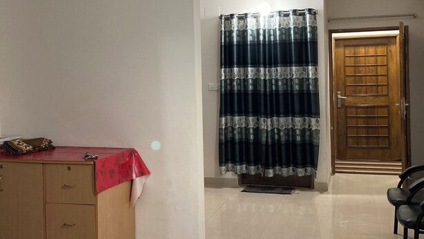 A room with a wooden cabinet, a red tablecloth-covered table, a patterned curtain, and a wooden door. - Appayan Guest House Baridhara (Dhaka)