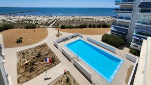 Een hotel met een zwembad, uitzicht op het strand en een hoog gebouw met balkons.