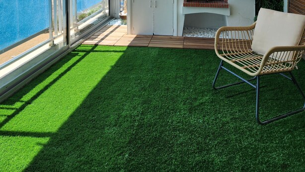 Een balkon met uitzicht op de oceaan, een plafondventilator, een bloempot, een barbecue en een rieten stoel.