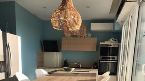 Een moderne keuken met een eethoek, met een houten tafel en stoelen, een hanglamp en uitzicht door een glazen deur.