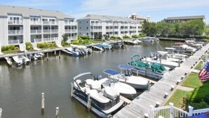 Un port de plaisance avec des bateaux amarrés, une jetée dotée d’une rambarde blanche et une rangée d’immeubles à plusieurs étages avec des balcons.
