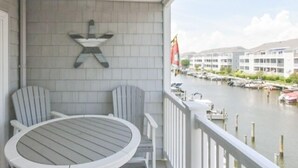 Un balcon avec une table ronde et deux chaises, donnant sur une marina où l’on peut admirer des bateaux et des bâtiments.