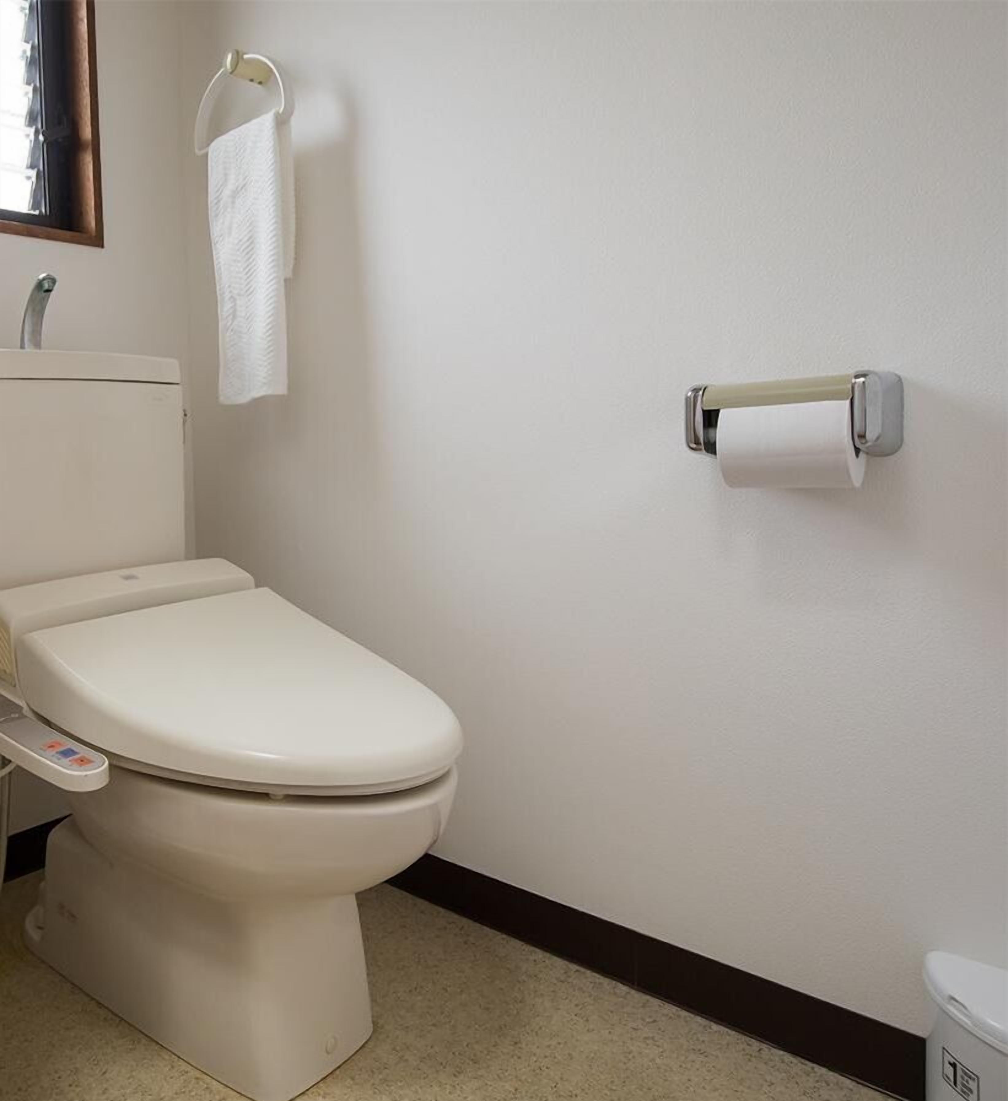 Un bagno standard con un water, un dispenser di carta assorbente e un asciugamano su un portasciugamani.
