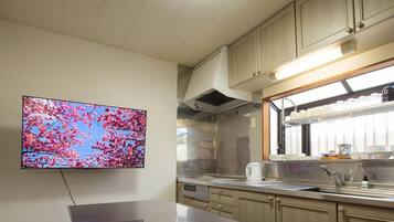 A modern kitchen with a flat-screen TV mounted on the wall, stainless steel appliances, and a window with a view of cherry blossoms.