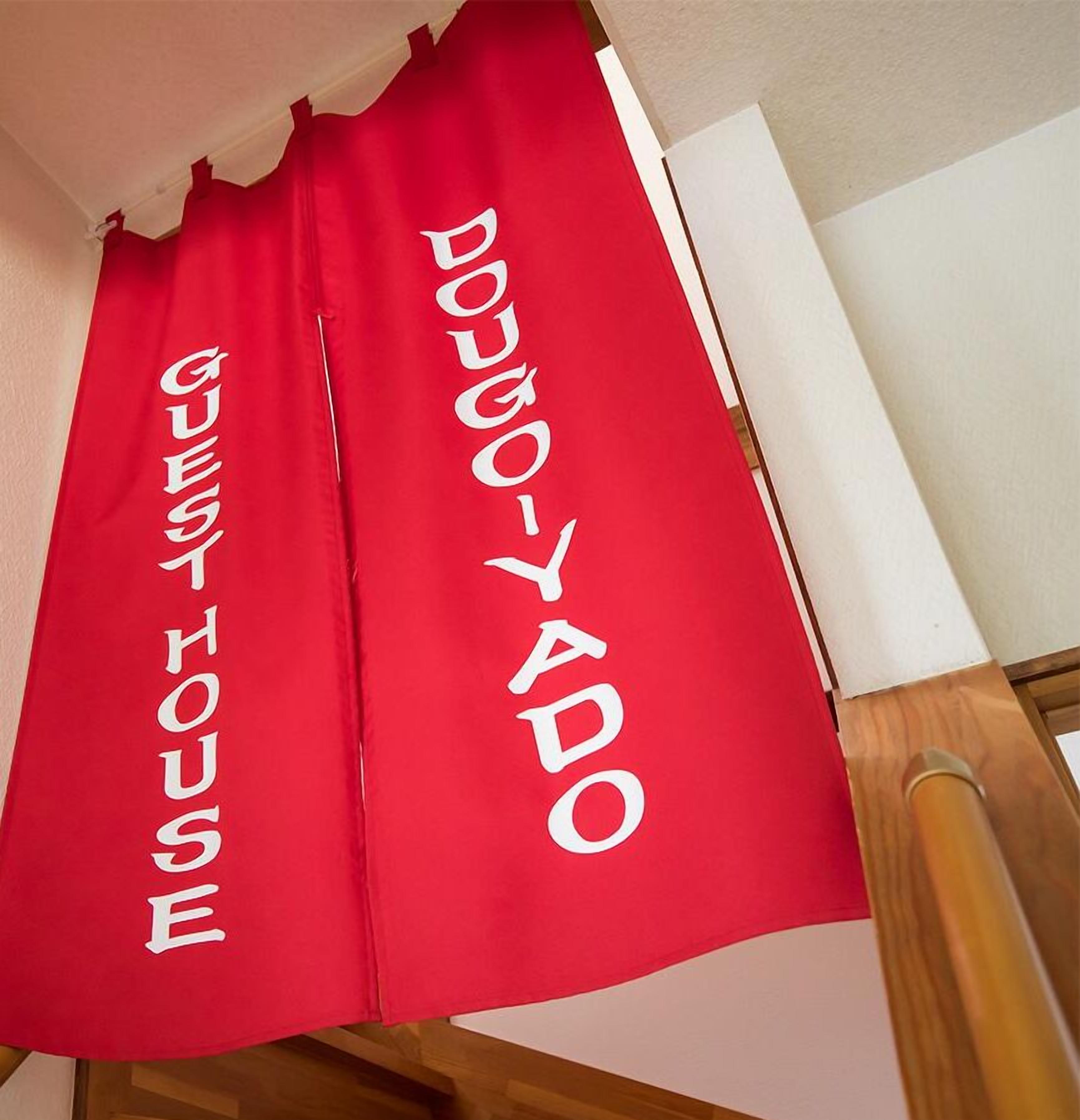 Un rideau rouge sur lequel sont inscrits les mots « GUEST HOUSE » et « DOUGYADO ».